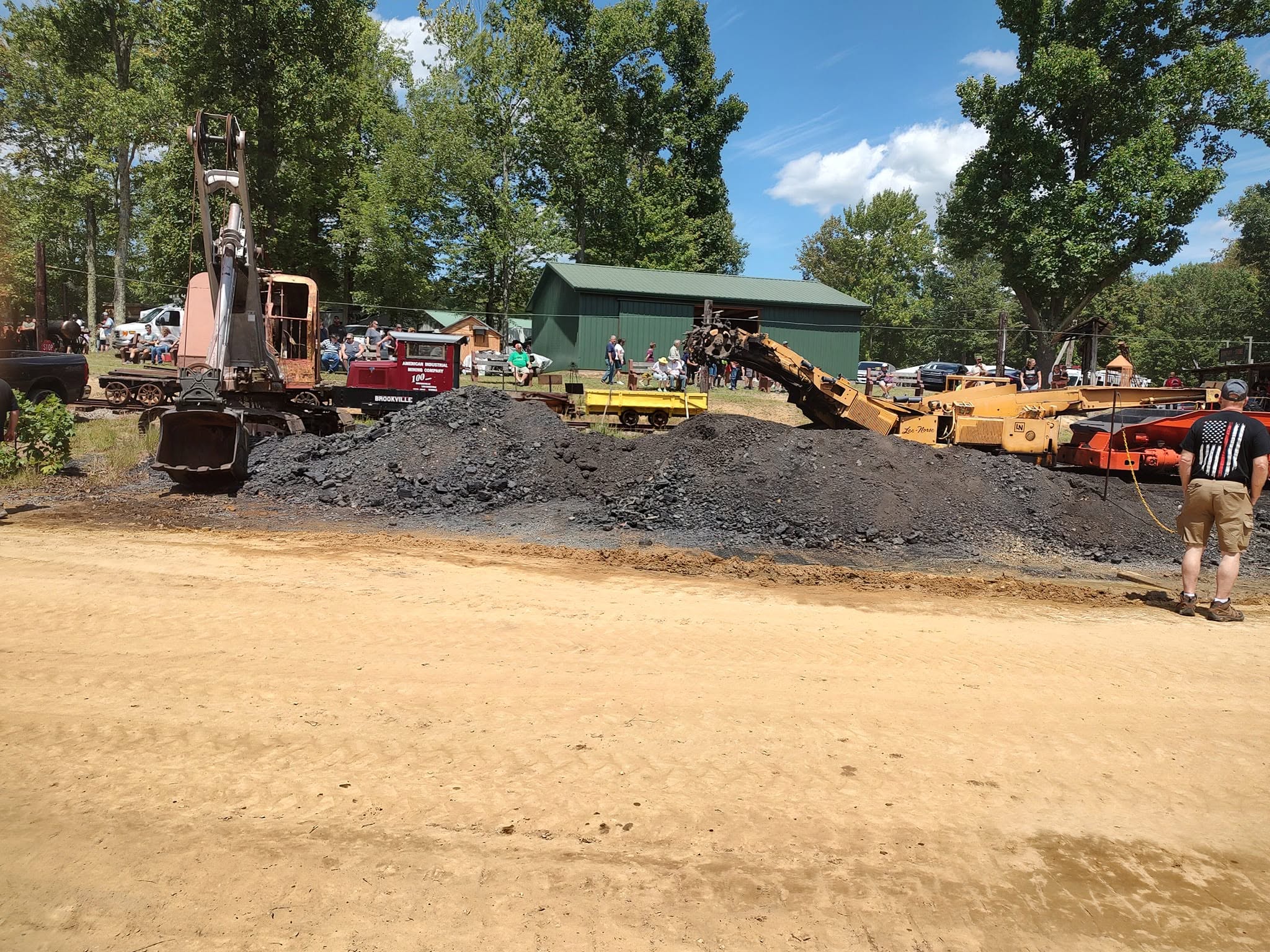 Vintage dragline shovel scooping material with a crowd watching from the edge of the field