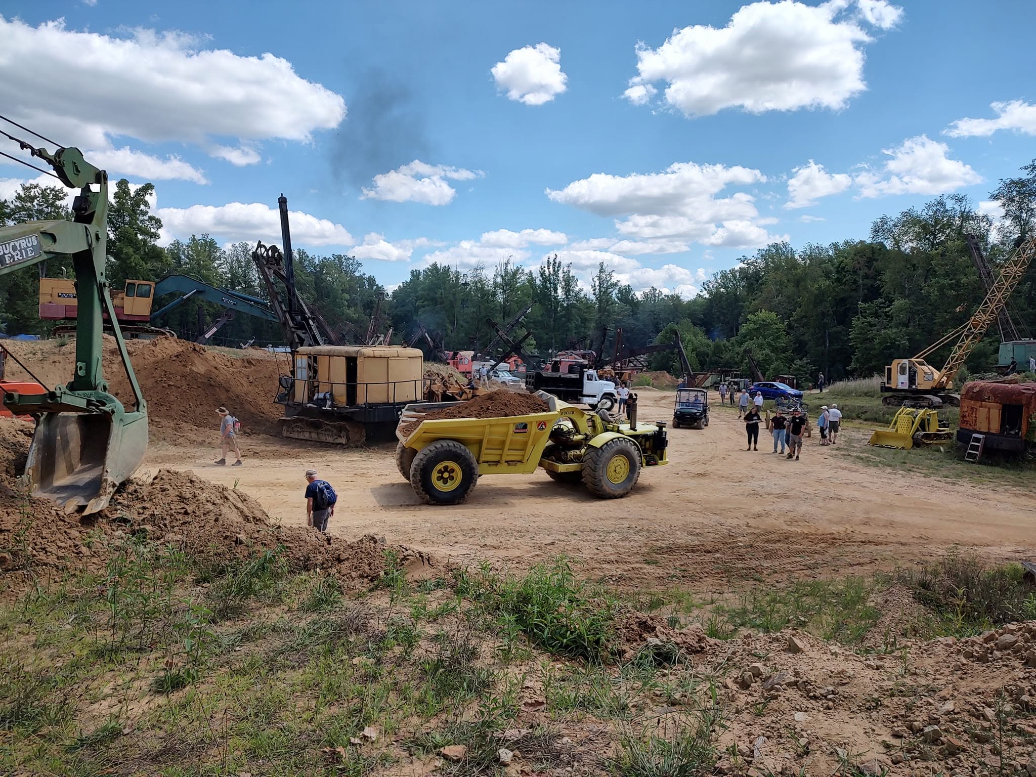 Yellow articulated dump truck among many pieces of vintage construction equipment on the demo field